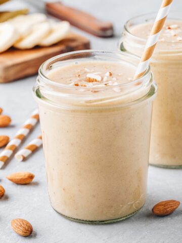 banana almond smoothie in a glass jar with a straw