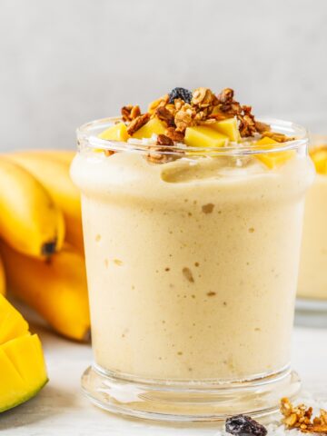 a glass of mango banana smoothie with granola and fruit