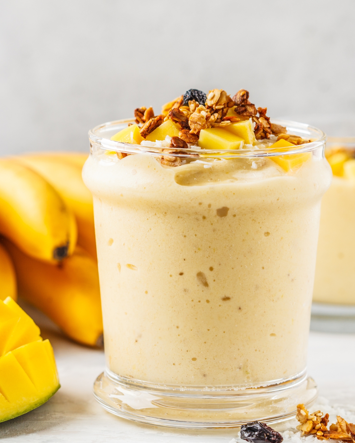 a glass of banana smoothie with mango, granola and fruit