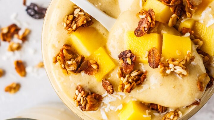 a glass of mango banana smoothie with granola and fruit