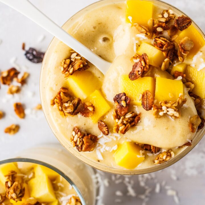 a glass of mango banana smoothie with granola and fruit