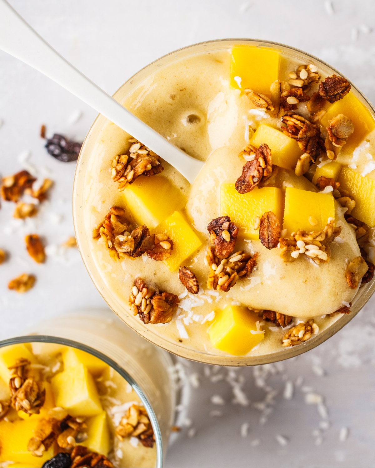 a glass of mango banana smoothie with granola and fruit