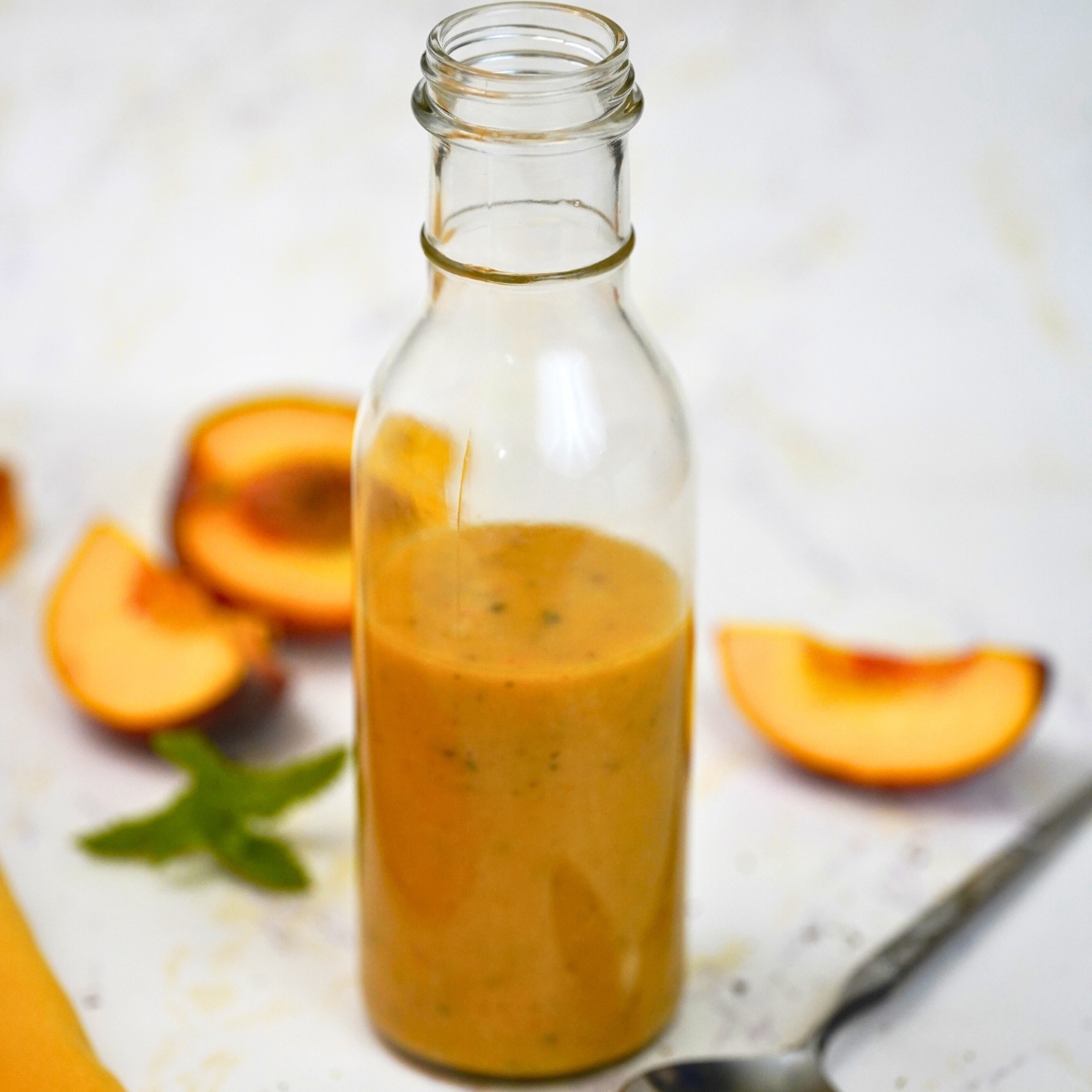 Peach mint vinaigrette in a bottle with peaches in the background