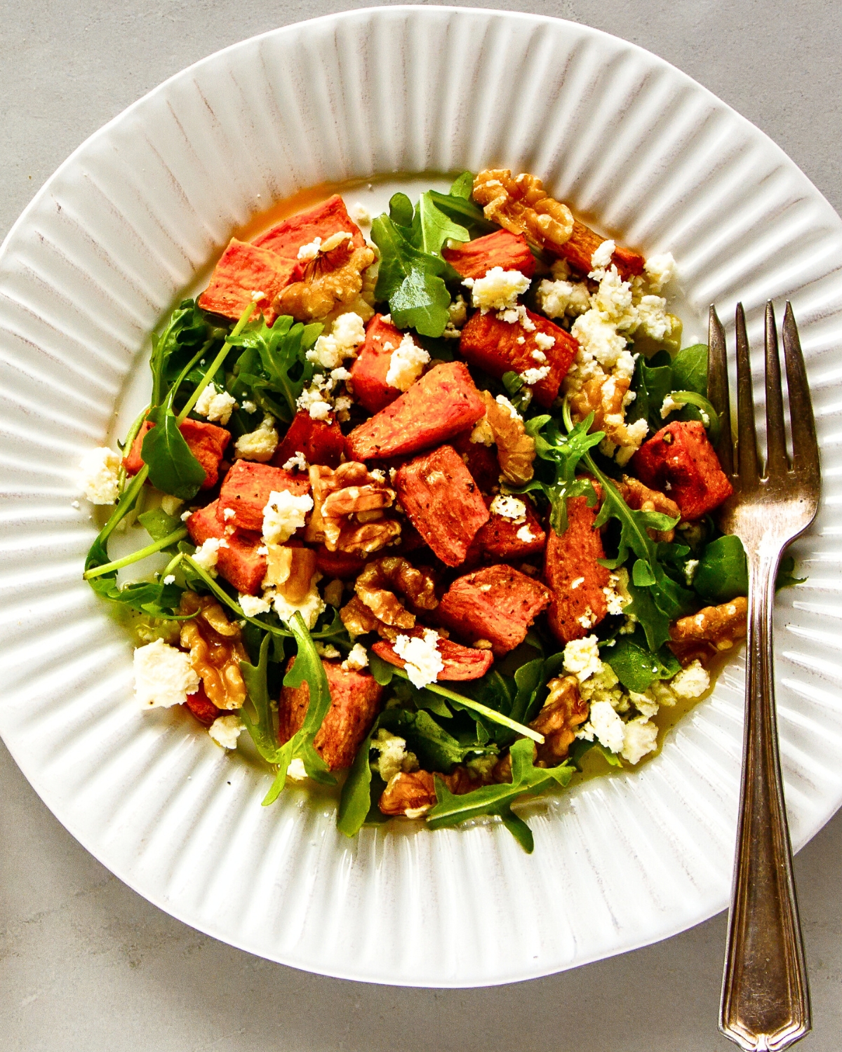 Sweet Potato and Arugula Salad with walnuts and feta cheese on a white plate