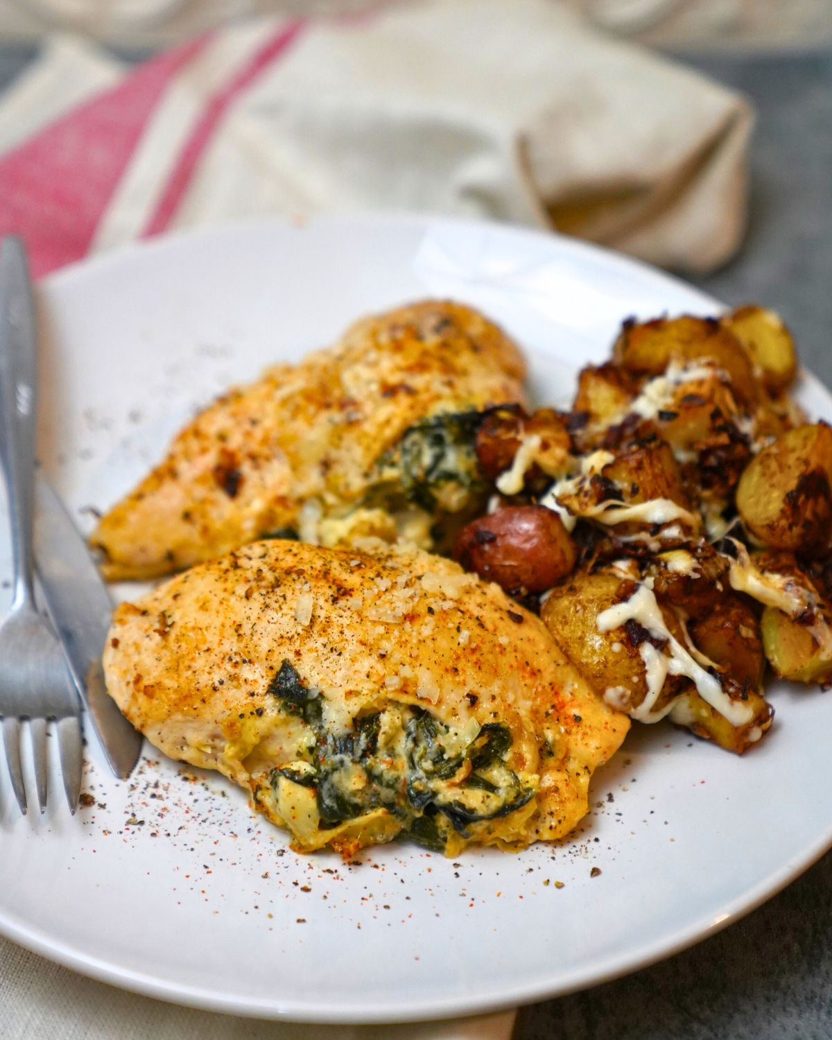 Spinach Artichoke Stuffed Chicken on a white plate with roasted onion potatoes